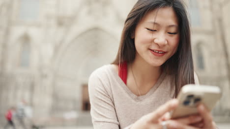 Chica-Asiática-Enviando-Mensajes-De-Texto-En-Un-Teléfono-Inteligente-Y-Esperando-A-Un-Amigo-Al-Aire-Libre.