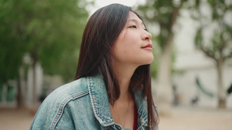 Asian-woman-taking-pictures-on-the-phone-while-sitting-on-a-bench-in-the-park.