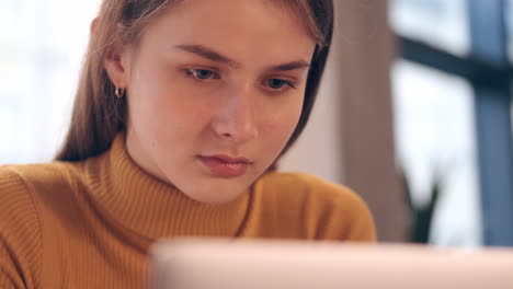 Close-up-shot-of-confident-student-girl-in-turtleneck-sweater-working-on-laptop-in-cafe.