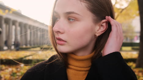 Portrait-of-Caucasian-girl-thoughtfully-posing-on-camera-in-city-park-at-sunset.