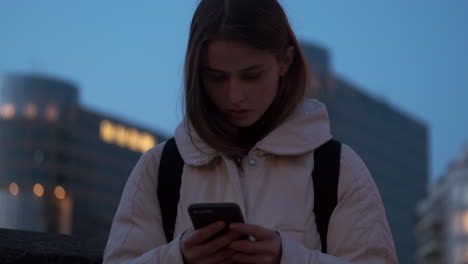 Kaukasisches-Mädchen,-Das-Selbstbewusst-Sein-Mobiltelefon-Benutzt-Und-Abends-Allein-In-Der-Stadt-Auf-Der-Straße-Steht.