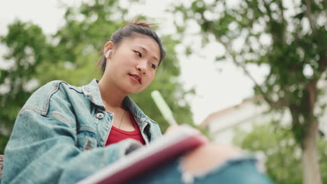 Asiatische-Frau-Schreibt-Im-Park-In-Ein-Notizbuch.