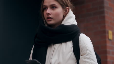 Close-up-tracking-shot-of-caucasian-girl-in-a-jacket-with-scarf-thoughtfully-walking-through-city-street.