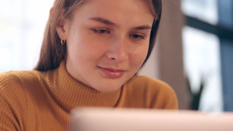 Close-up-view-of-Caucasian-student-girl-happily-working-on-laptop-in-cafe.