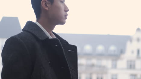 Young-Asian-businessman-in-coat-waiting-public-transport-on-street.