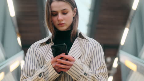 Retrato-De-Una-Niña-Caucásica-Usando-Atentamente-Un-Teléfono-Celular-En-Las-Escaleras-De-La-Estación-De-Metro.