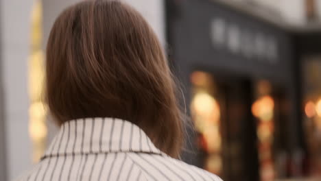 Vista-Posterior-De-Una-Elegante-Chica-Caucásica-Con-Gabardina-Caminando-Sola-Y-Con-Confianza-Por-Las-Calles-De-La-Ciudad.