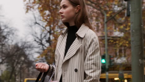 Tracking-shot-of-stylish-Caucasian-girl-in-trench-coat-waiting-at-a-traffic-light.