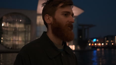 Young-smiling-redhead-bearded-man-happily-looking-in-camera-on-city-street-at-night.