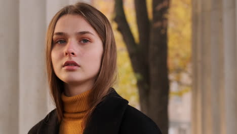 Tracking-shot-of-stylish-Caucasian-girl-in-coat-confidently-walking-through-city-street-at-sunset.