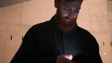 Tracking-around-shot-of-young-bearded-man-confidently-using-cellphone-on-city-street-at-night-outside-business-center.