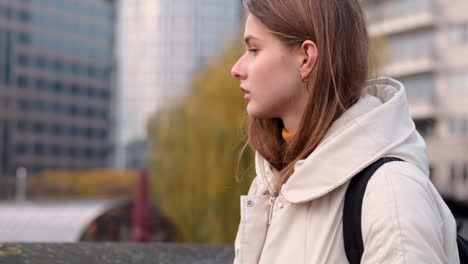 Caucasian-girl-in-down-jacket-with-backpack-walking-through-city-street.