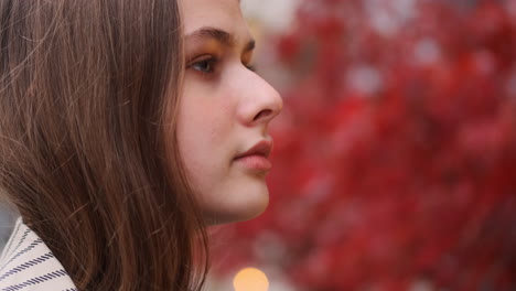 Close-up-shot-of-Caucasian-girl-in-trench-coat-thoughtfully-looking-aside-on-city-street.