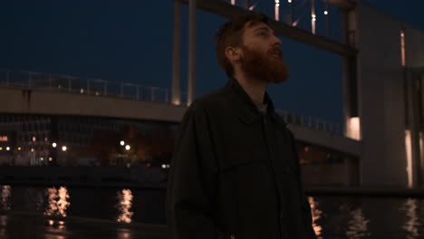 Young-redhead-bearded-man-thoughtfully-walking-through-city-street-at-night.