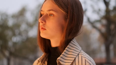 Close-up-shot-of-pensive-girl-in-trench-coat-dreaming-near-fashion-store-on-city-street.