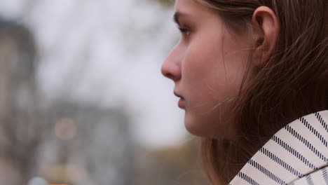 Close-up-tracking-shot-of-stylish-girl-in-coat-waiting-traffic-light-on-city-street.