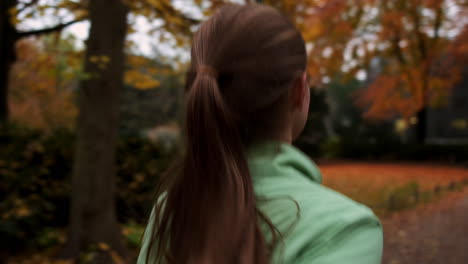 Tracking-around-shot-of-sporty-Caucasian-girl-running-alone-in-beautiful-autumn-city-park.