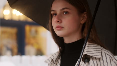 Portrait-of-stylish-Caucasian-girl-in-trench-coat-with-umbrella-walking-through-rainy-city-street.