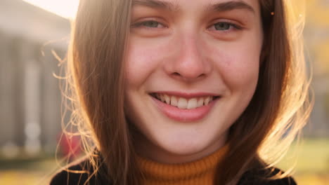 Close-up-portrait-shot-of-pretty-smiling-girl-joyfully-looking-in-camera-outdoor-at-sunset.