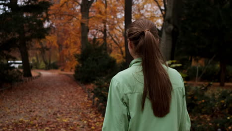 Back-view-of-sporty-Caucasian-girl-walking-after-running-in-colorful-autumn-city-park.