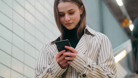 Chica-Caucásica-Sonriente-Usando-Soñadoramente-Un-Teléfono-Celular-En-Las-Escaleras-De-La-Estación-De-Metro.