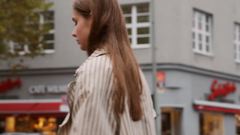 Tracking-in-shot-of-stylish-Caucasian-girl-in-trench-coat-walking-through-rainy-city-street.