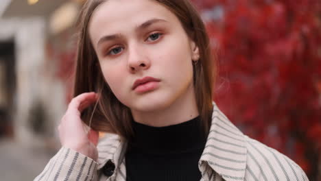 Portrait-of-Caucasian-girl-in-trench-coat-intently-looking-in-camera-on-city-street.