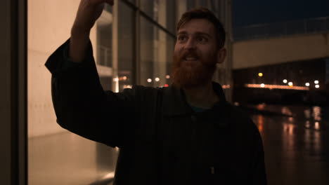 Tracking-around-shot-of-young-attractive-bearded-man-happily-talking-on-video-chat-on-cellphone-on-city-street-at-night.