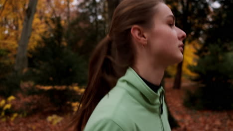 Tracking-of-sporty-Caucasian-girl-dreamily-running-in-colorful-autumn-city-park.