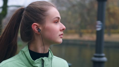 Chica-Caucásica-Deportista-Con-Auriculares-Caminando-Soñadoramente-Después-De-Correr-En-El-Parque-De-La-Ciudad-Junto-Al-Río.