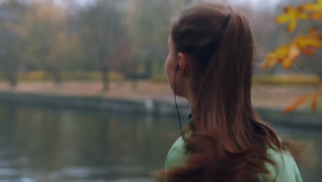 Back-view-of-sporty-Caucasian-girl-in-earphones-running-in-autumn-city-park.