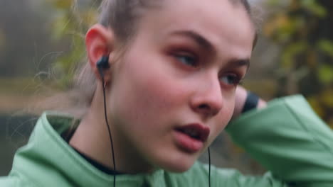 Close-up-shot-of-sporty-Caucasian-girl-in-earphones-confidently-walking-after-running-in-city-park-on-riverside.