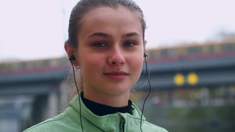 Retrato-De-Una-Sonriente-Niña-Caucásica-Deportista-Con-Auriculares-Mirando-Felizmente-A-La-Cámara-En-El-Parque-De-La-Ciudad.