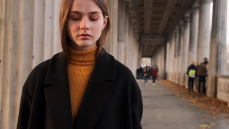 Tracking-shot-of-stylish-Caucasian-girl-in-coat-confidently-walking-through-archway-in-city-park-at-sunset.