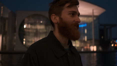 Joven-Pelirrojo-Y-Barbudo-Sonriente-Mirando-Alegremente-A-La-Cámara-En-La-Calle-De-La-Ciudad-Por-La-Noche.