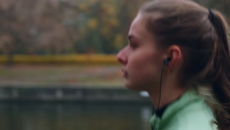 Tracking-shot-of-sporty-Caucasian-girl-in-earphones-dreamily-running-in-autumn-city-park.