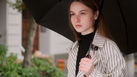 Medium-shot-of-stylish-Caucasian-girl-in-trench-coat-with-umbrella-on-rainy-city-street.