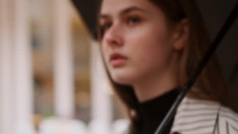 Close-up-shot-of-stylish-Caucasian-girl-with-umbrella-walking-alone-through-rainy-city-street.