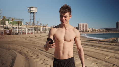 Tracking-out-shot-of-young-attractive-sporty-man-taking-selfie-on-smartphone-after-workout-on-sport-ground