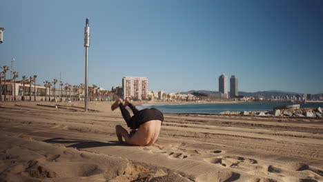 Joven-Musculoso-Haciendo-Ejercicio-Acrobático-Durante-El-Entrenamiento-Junto-Al-Mar