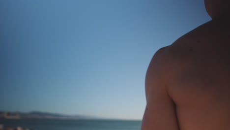 Tracking-around-shot-of-young-confident-muscular-man-resting-after-workout-on-beach