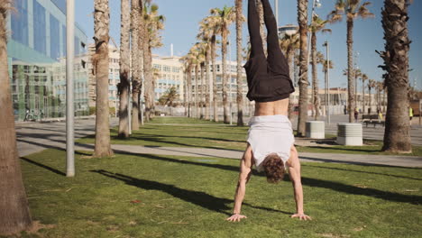 Tracking-shot-of-young-sporty-man-standing-on-hands-during-workout-outdoor