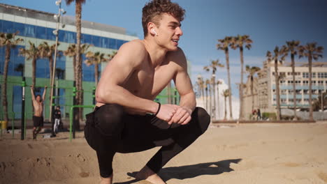 Young-attractive-muscular-man-resting-after-hard-workout-on-sport-ground-on-beach