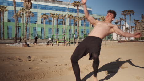 Tracking-shot-of-young-muscular-man-doing-somersault-or-side-flip-on-city-beach