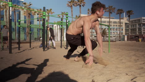 Joven-Musculoso-Haciendo-Ejercicios-Duros-Durante-El-Entrenamiento-Funcional-En-El-Campo-Deportivo-De-La-Playa