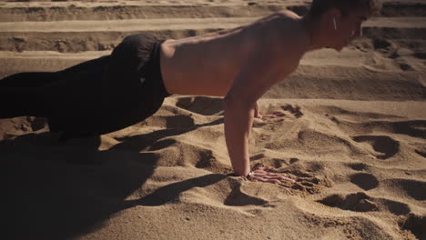 Tracking-shot-of-handsome-fit-guy-pushing-up-during-functional-training-on-beach