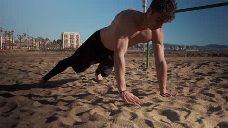 Joven-Fuerte-Y-Musculoso-Haciendo-Ejercicios-Duros-Durante-El-Entrenamiento-Funcional-En-La-Playa-De-La-Ciudad