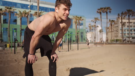 Young-sporty-muscular-man-resting-after-hard-workout-on-sport-ground-outdoor