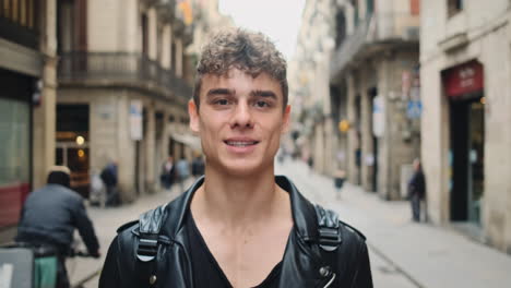 Tracking-out-shot-of-young-attractive-smiling-man-joyfully-looking-in-camera-on-city-street