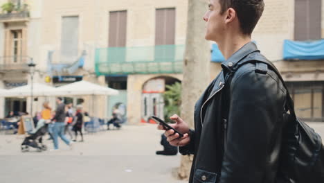 Tracking-around-shot-of-young-attractive-man-with-smartphone-thoughtfully-standing-on-street